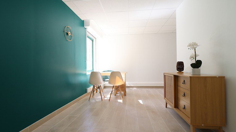 Espace clair avec mur vert, commode en bois et chaises.
